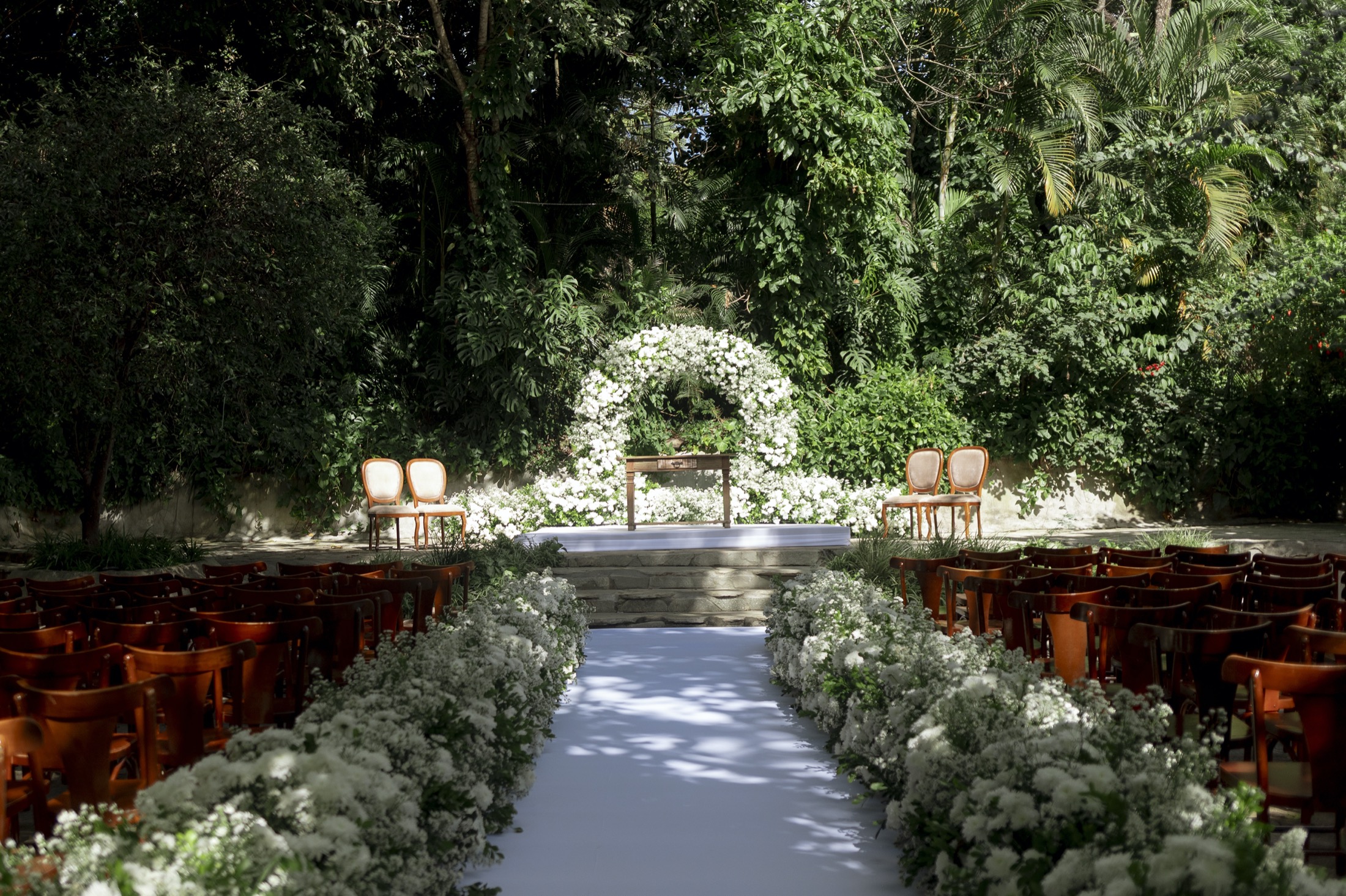 Corredor de cerimônia decorado com flores brancas e arco floral em meio à floresta no Sítio Geranium